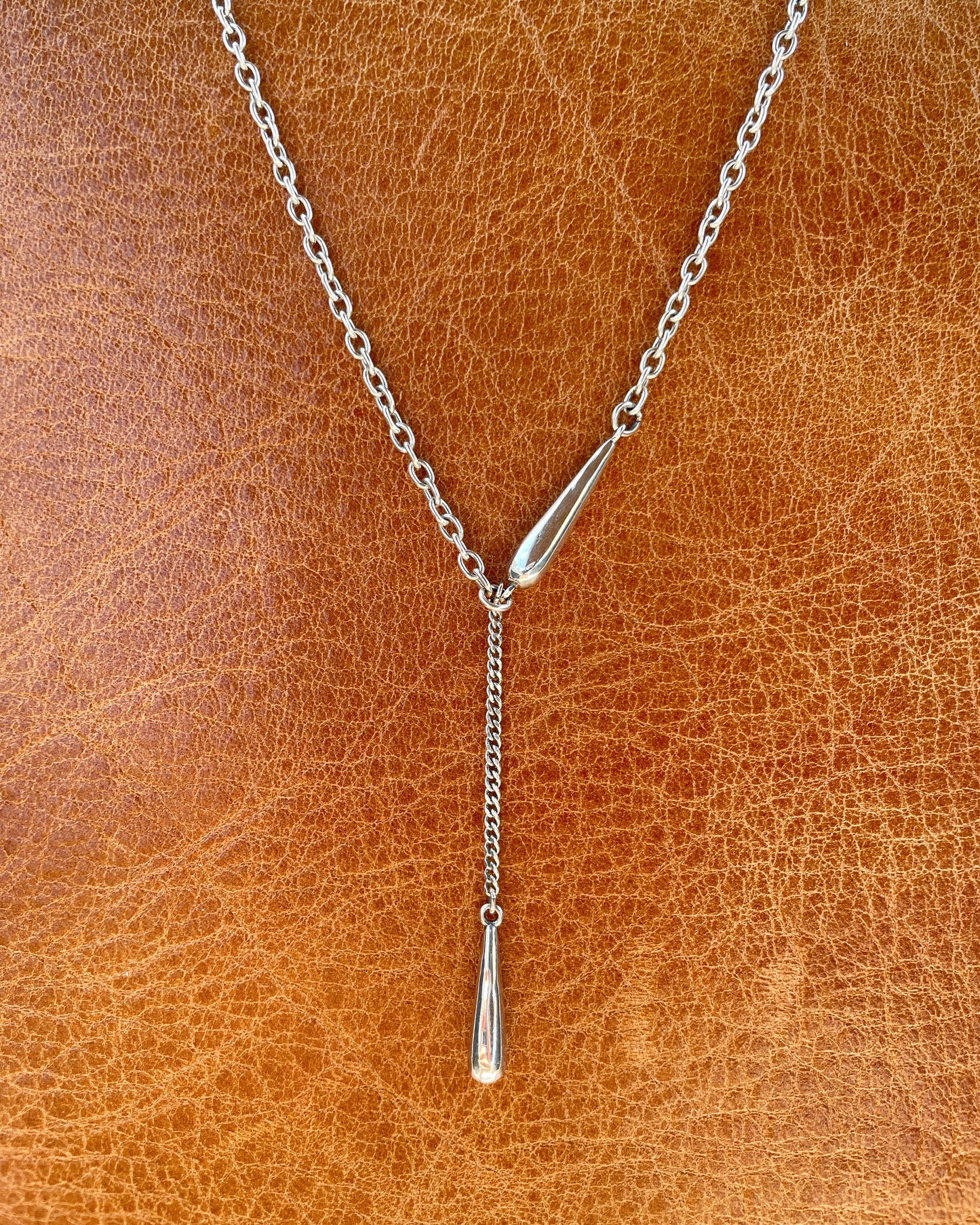 Modern silver necklace with long drop charm – styled flatlay
