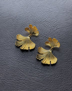 Layered gold ginkgo leaf earrings on leather background