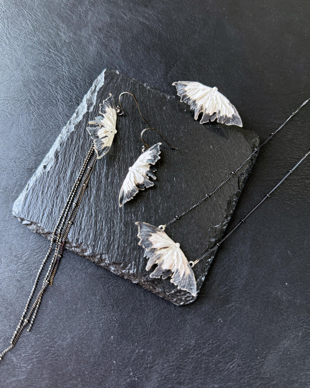 Soul Moth earrings and necklace laid on black stone